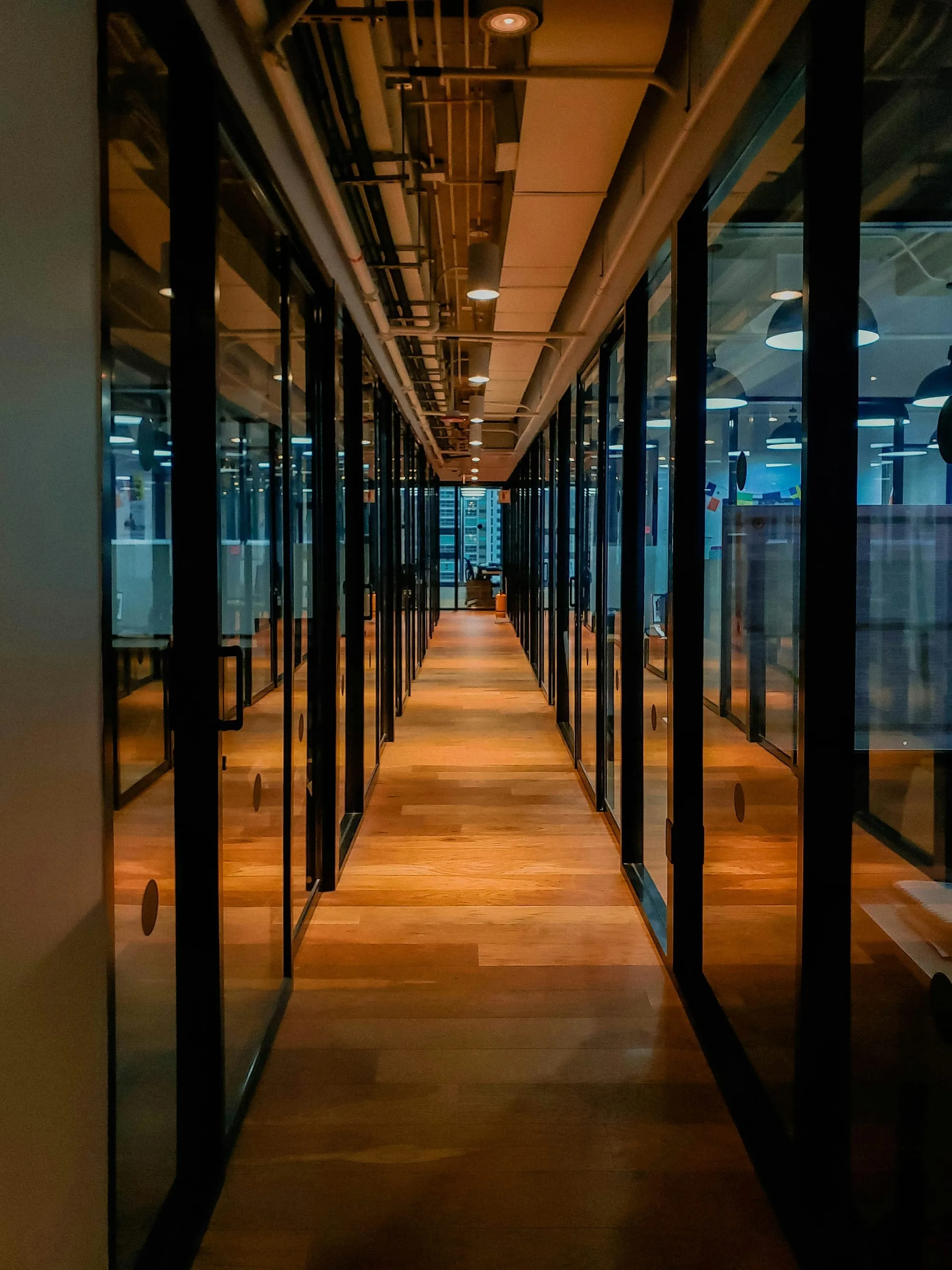 An empty office corridor lined with glass-walled meeting rooms