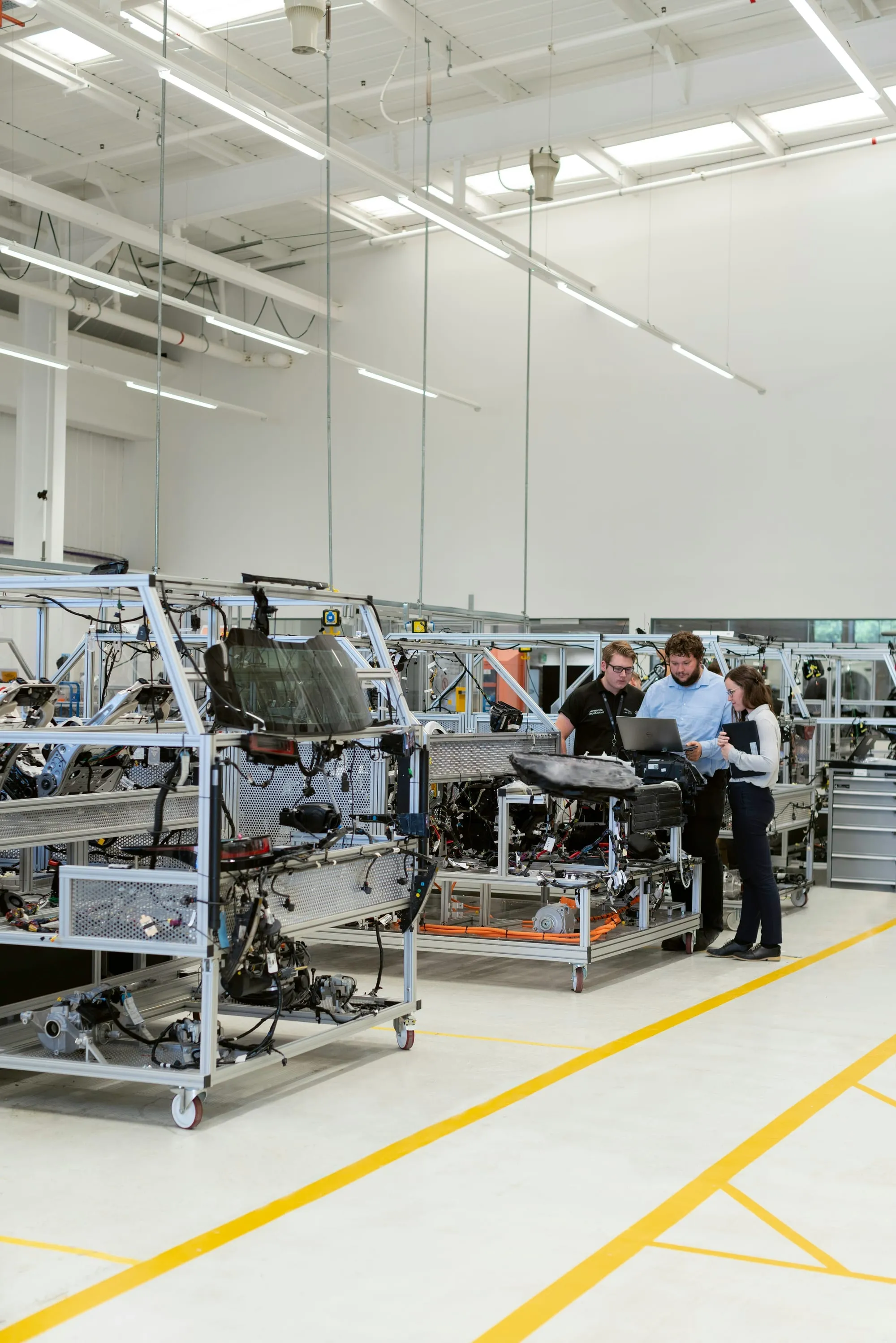 A bright assembly hall with workstations on yellow-lined floors and technicians at the far end