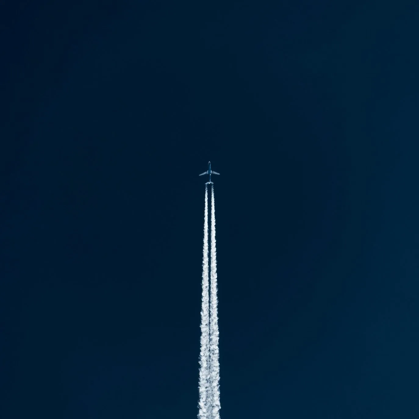 An airplane flying overhead leaving contrails in a blue sky