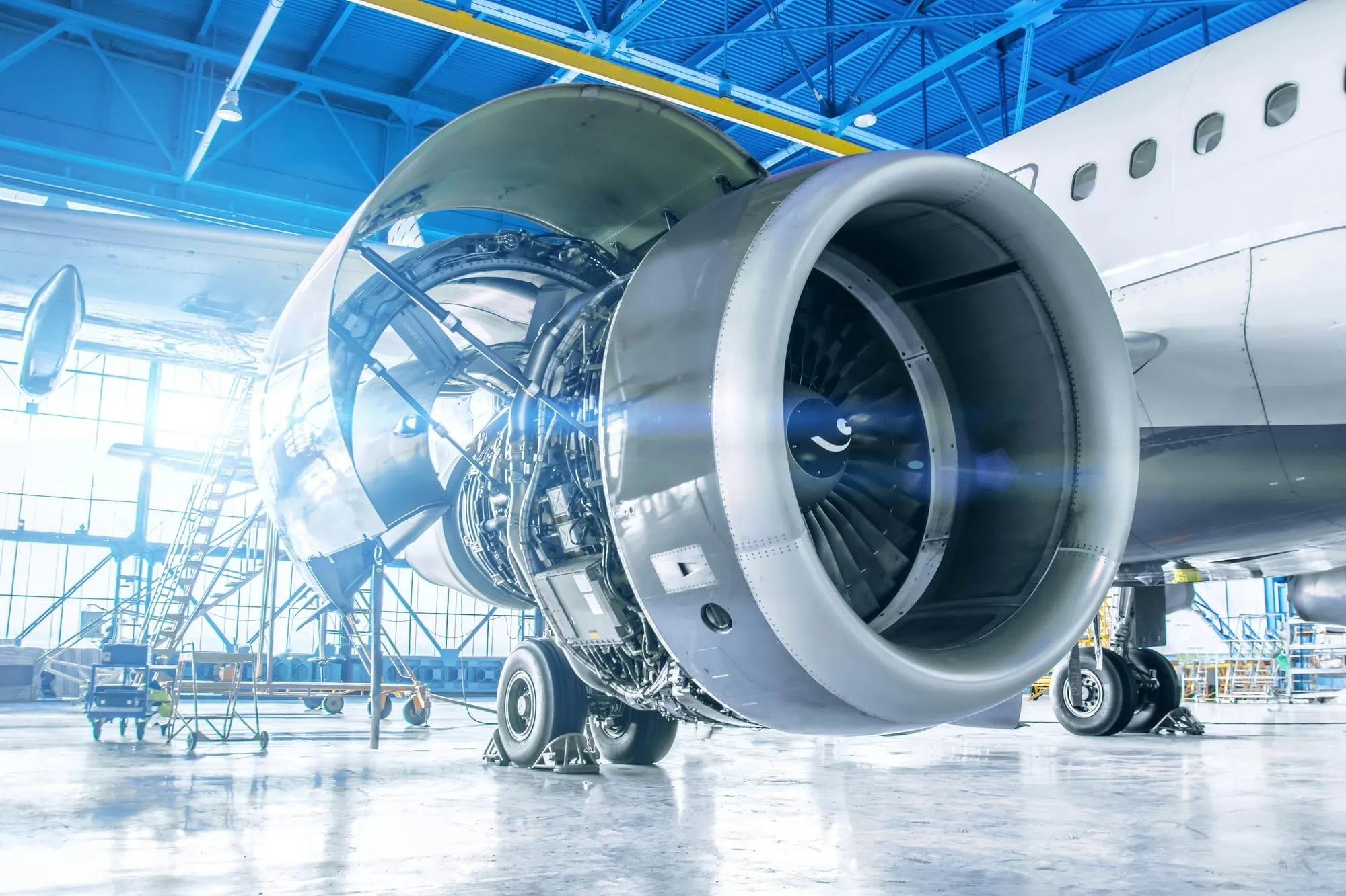 A jet engine with its cowling open on an aircraft parked in a maintenance hangar